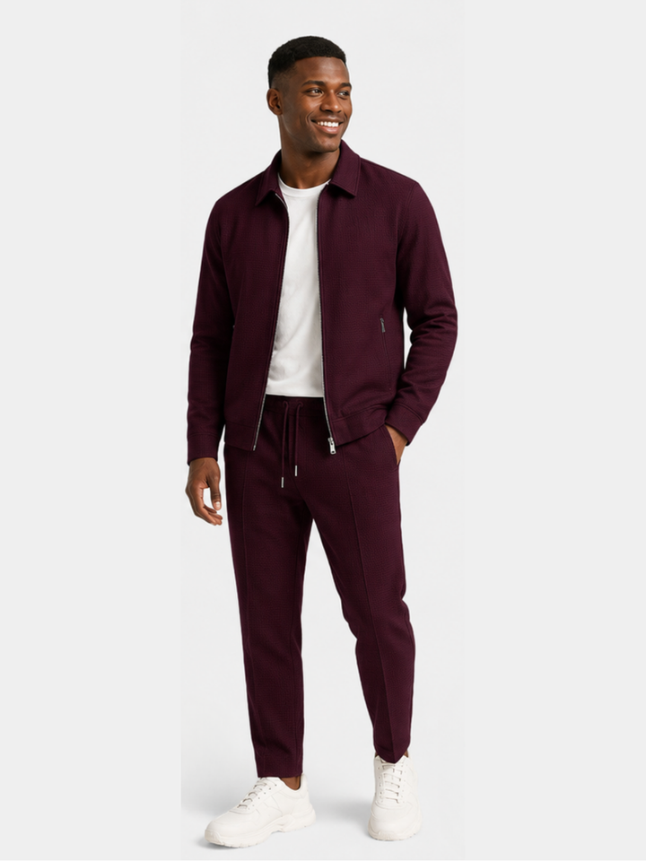 Burgundy jacket and jogger pants set worn with white sneakers, standing pose