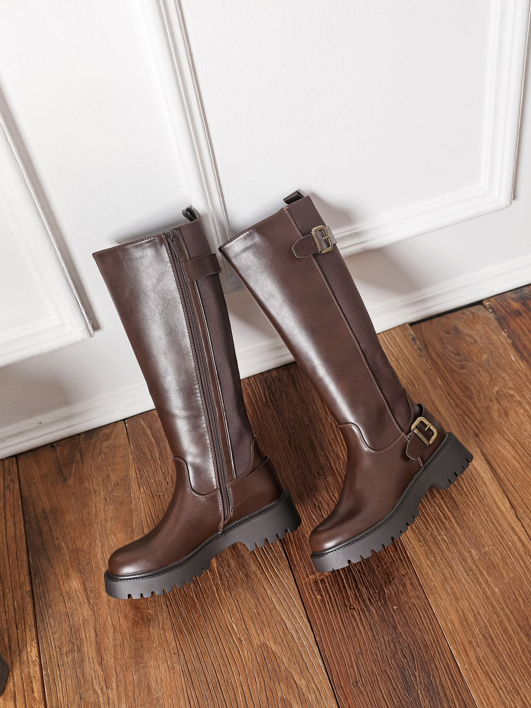 Pair of brown leather-look knee high boots leaning against a white door