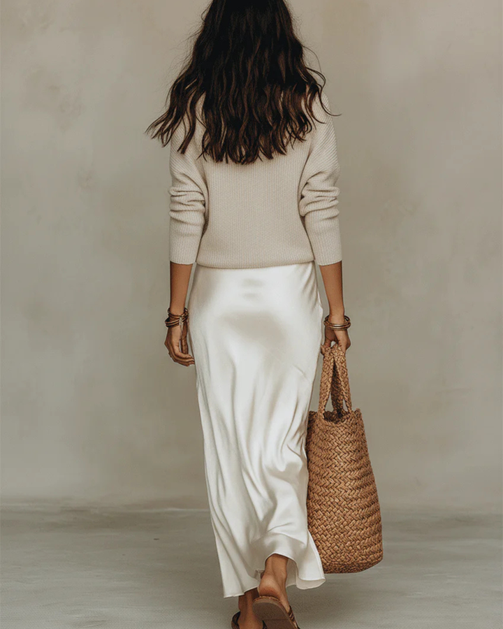 Back view of the ivory satin midi dress with beige sweater and tote bag