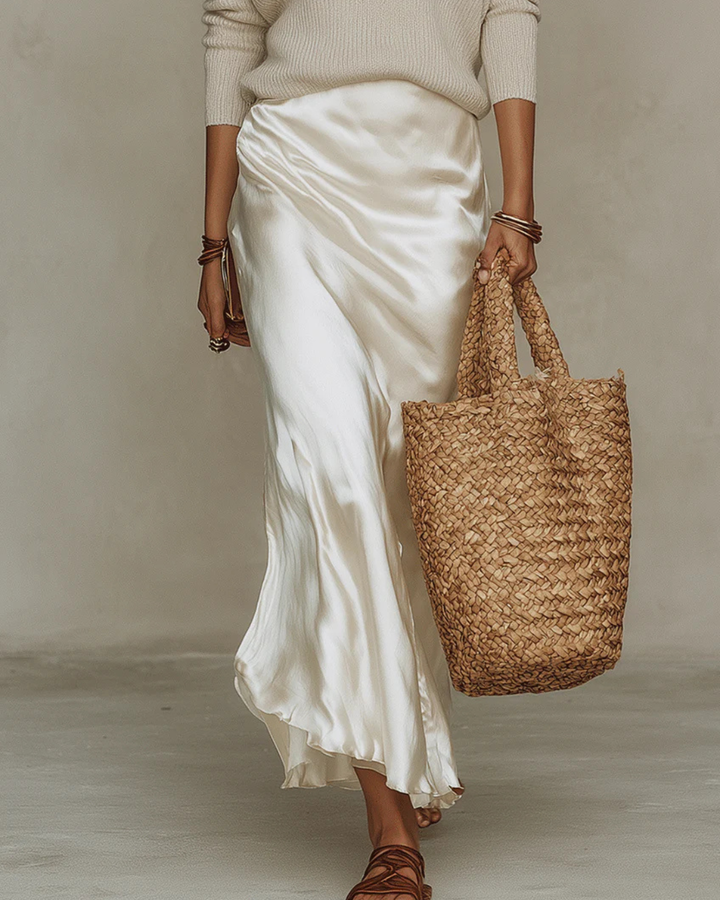 Ivory satin midi skirt hem flowing while walking, with woven tote bag