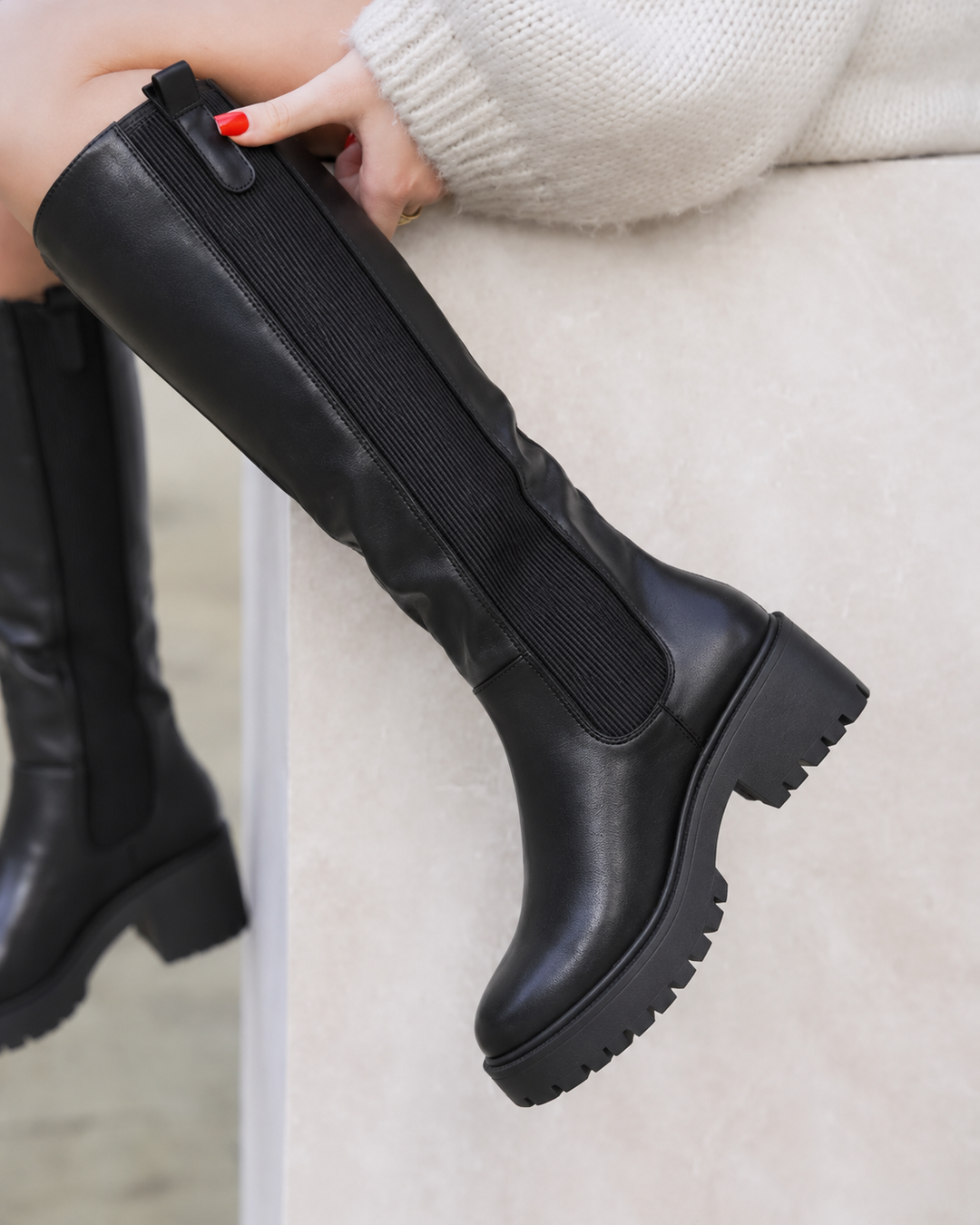 Women's black knee high boots with platform lug sole, seated side view