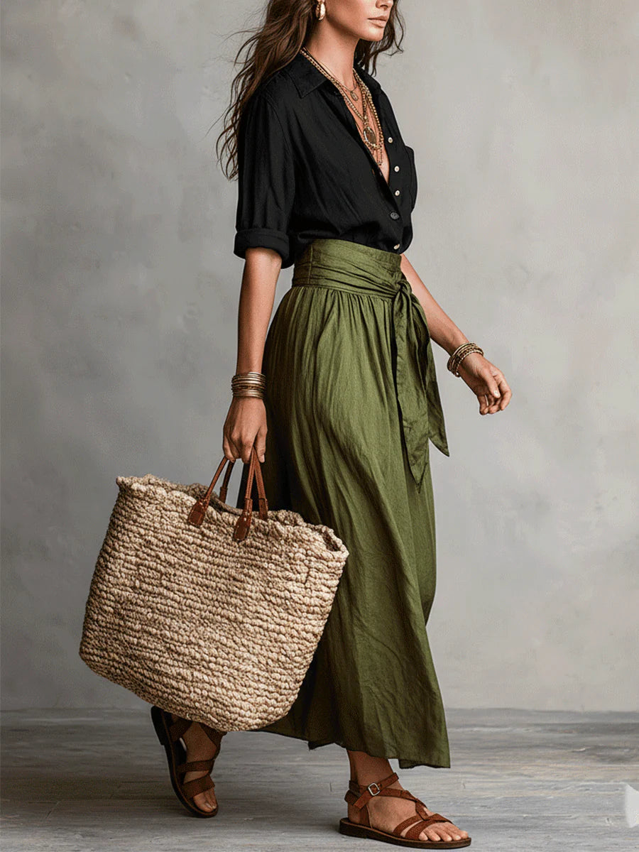 Side view of the olive wrap midi skirt with a tie waist, carrying a straw bag