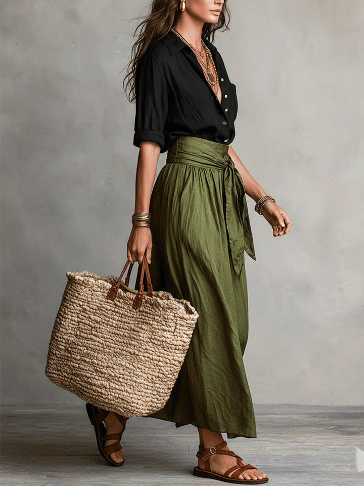 Side view of the olive wrap midi skirt with a tie waist, carrying a straw bag