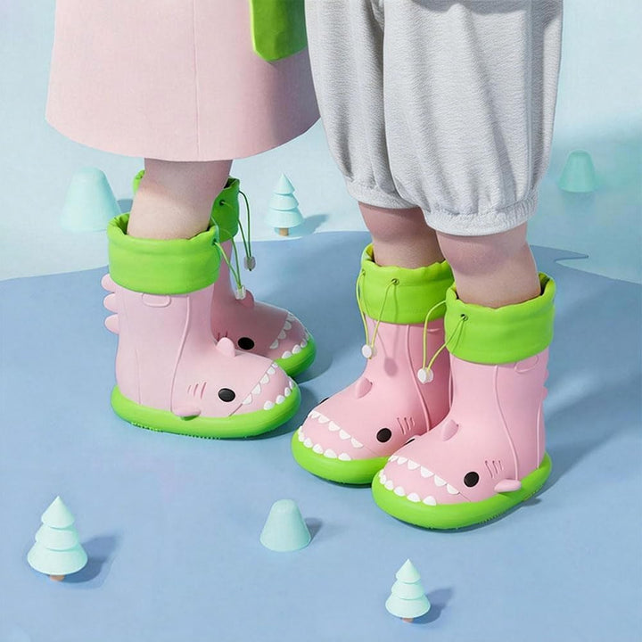 Toddler wearing pink shark rain boots with green drawstring cuffs