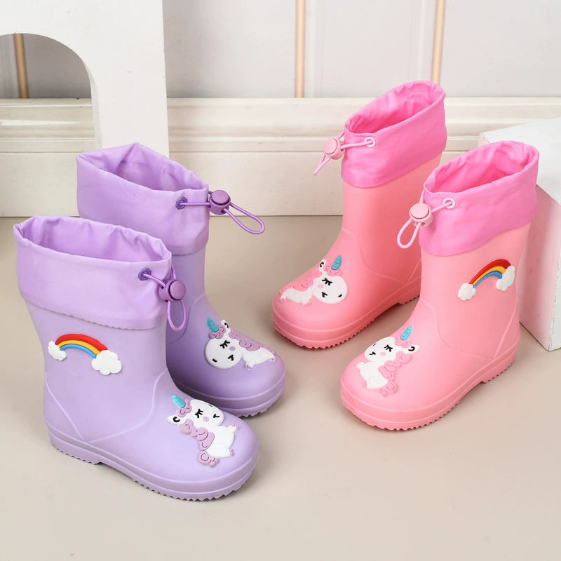 Purple and pink unicorn rain boots with rainbow patches on a play room floor