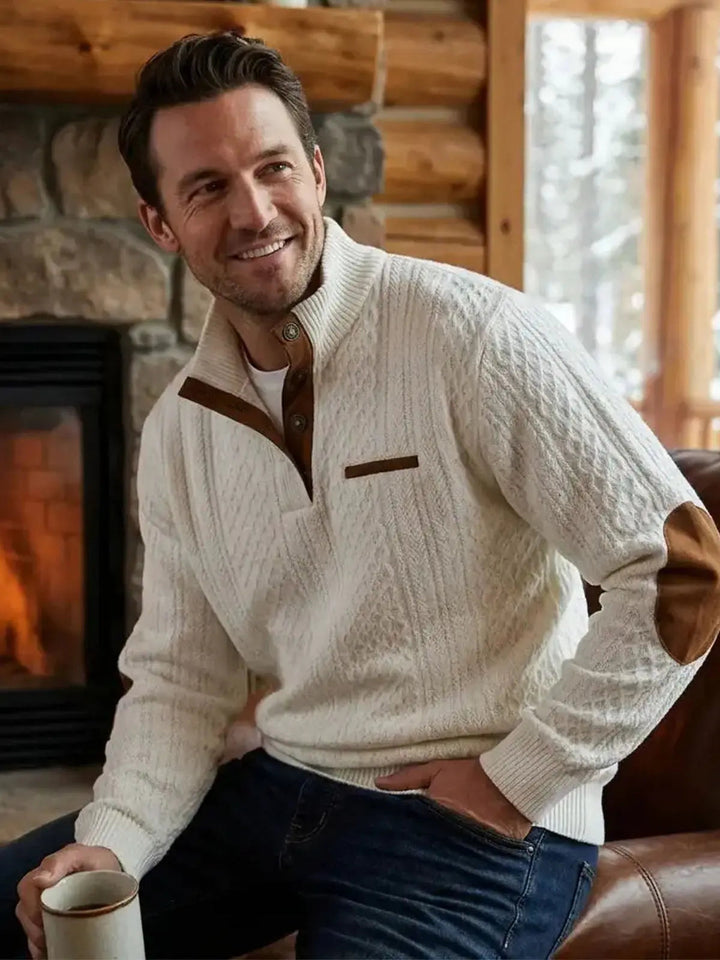 Smiling man in the white cable knit sweater sitting by a fireplace