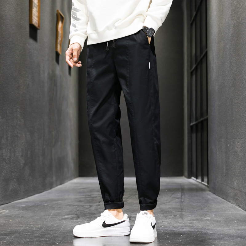 Black tapered joggers with drawstring and cuffed ankles, worn with white sweater