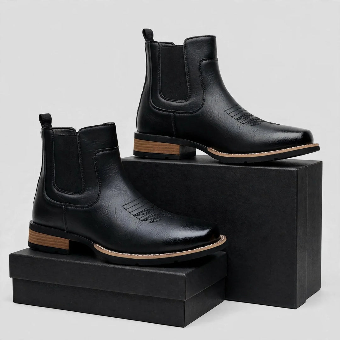 Pair of black pull-on boots staged on black boxes in a studio