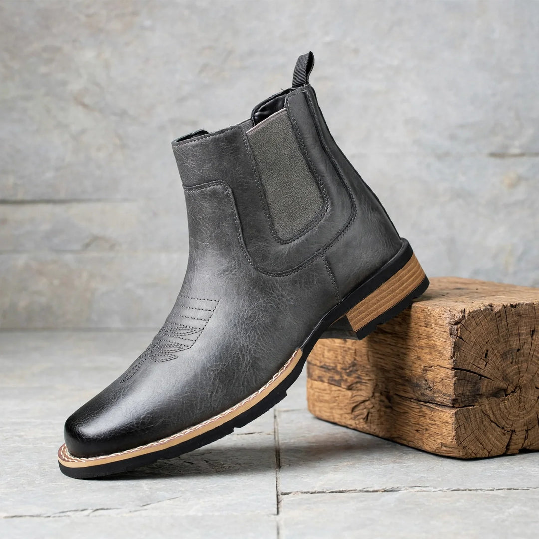 Gray Chelsea boot with stitched toe, side view beside a wooden block