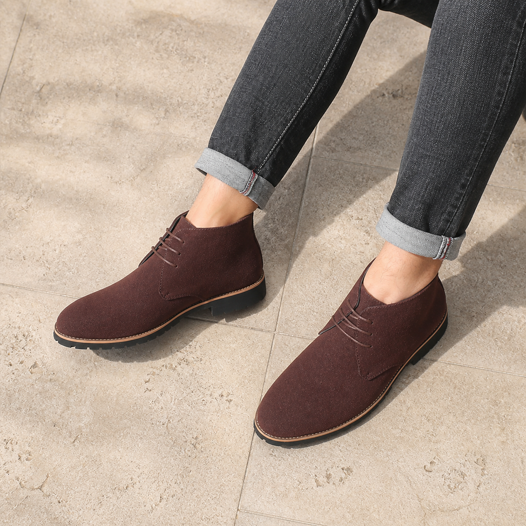Chocolate chukka boots worn with rolled gray jeans while seated