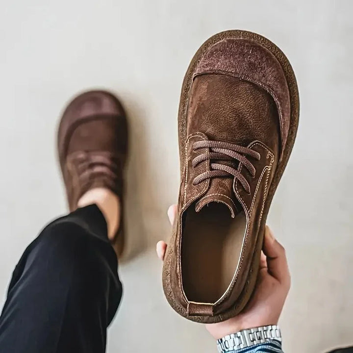 Top view of a brown wide toe lace up shoe held in hand next to a worn shoe