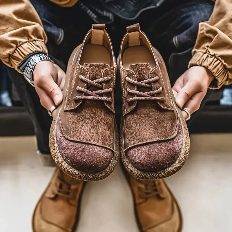 Hands holding a pair of brown wide toe lace up shoes