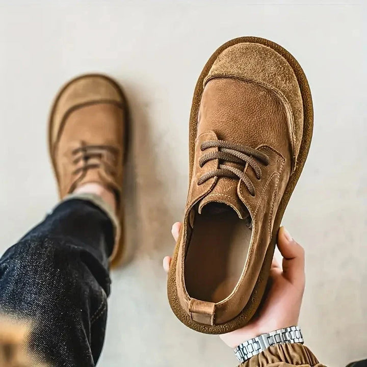 Top view of a tan wide toe lace up shoe held in hand next to a worn shoe