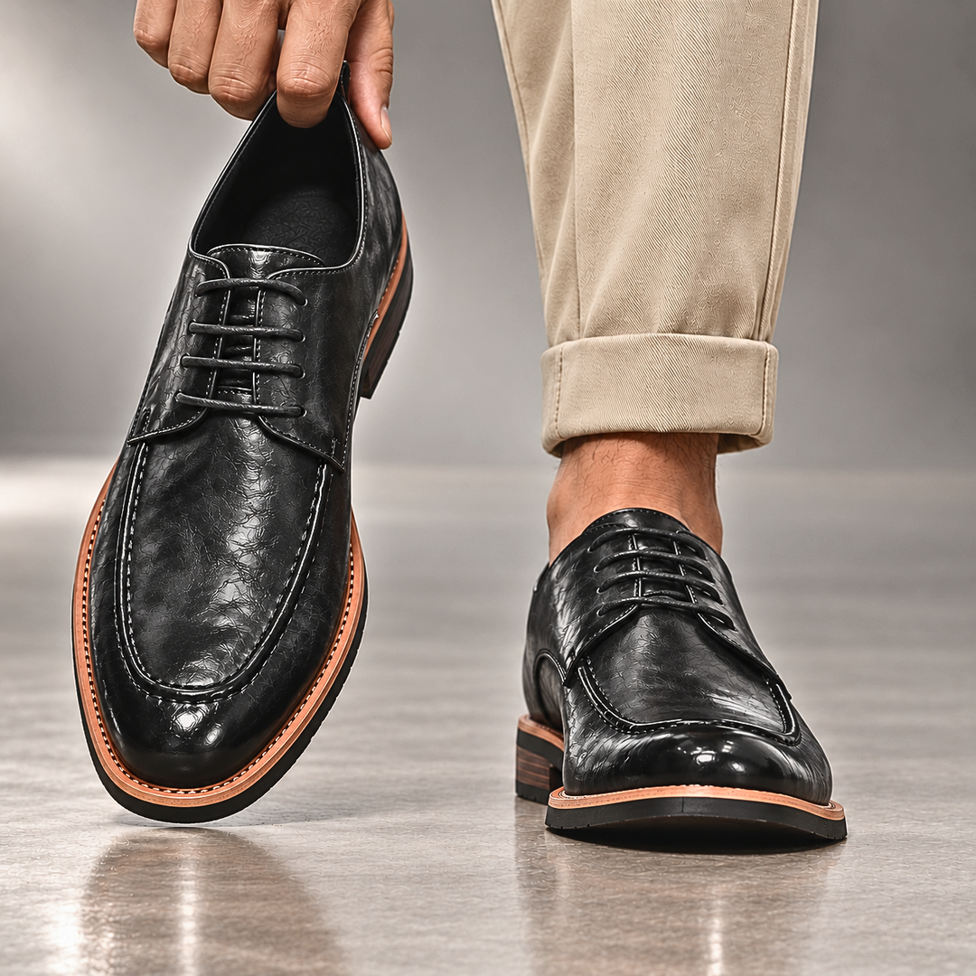 Hand holding a black derby shoe next to beige cuffed trousers