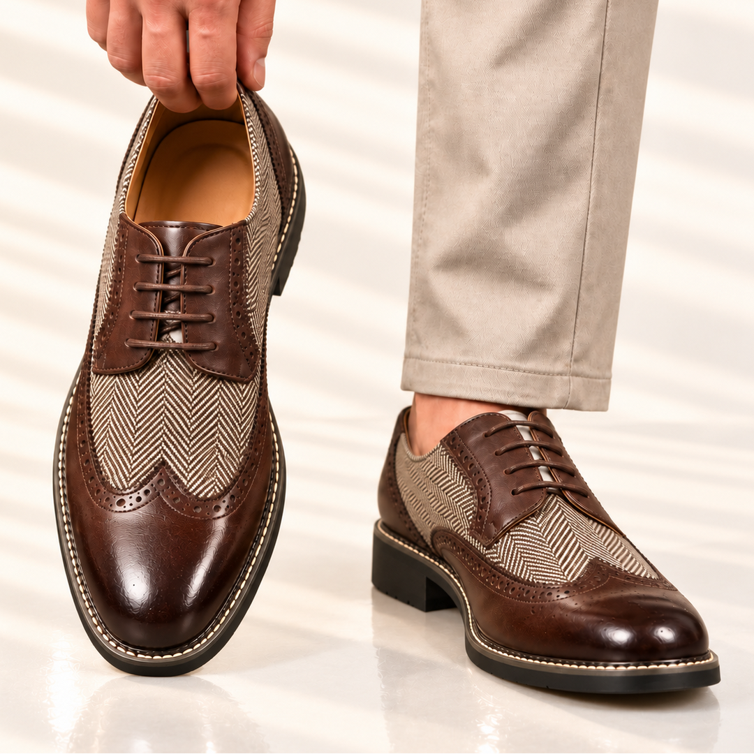 Brown wingtip brogues held up by hand, with beige trousers and a second shoe worn