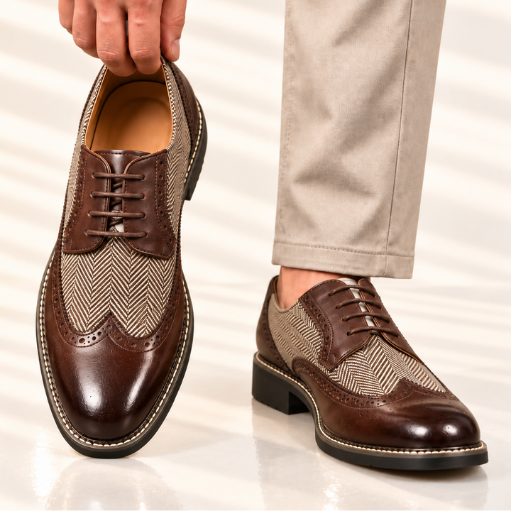 Brown wingtip brogues held up by hand, with beige trousers and a second shoe worn
