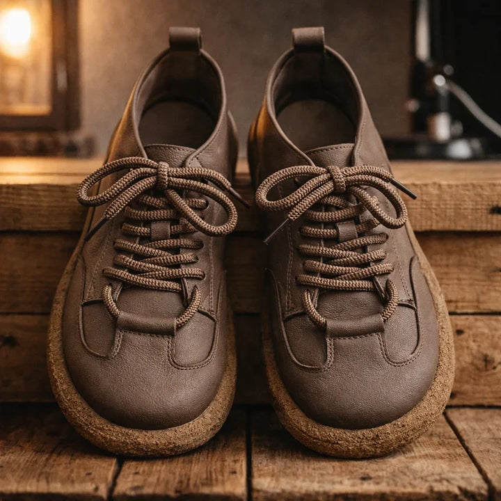 Pair of taupe wide toe lace up sneakers on a wooden shelf