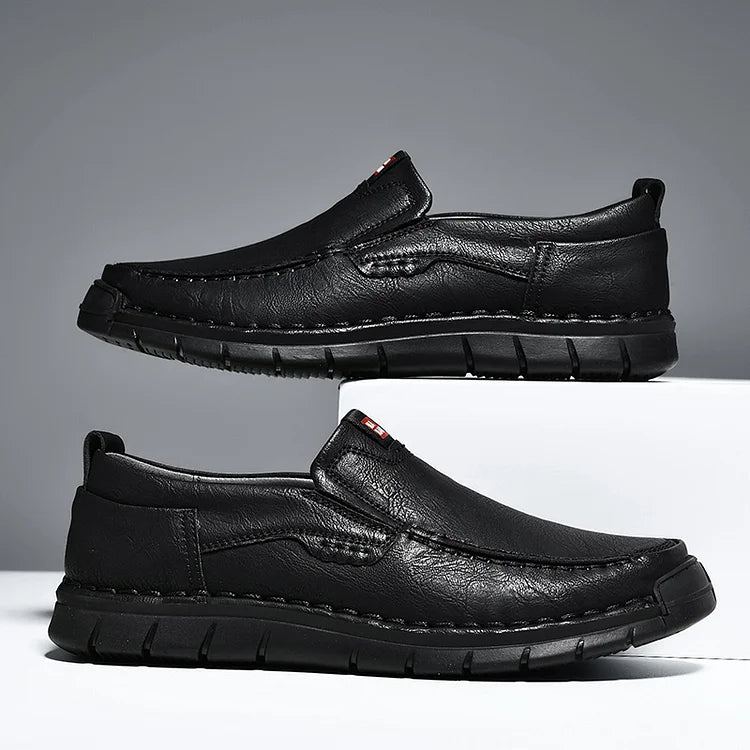 Pair of black slip on loafers with stitched detail on a white block