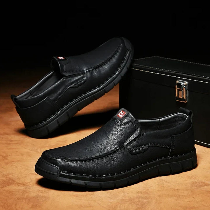 Pair of black slip on loafers with stitched toe on a dark background