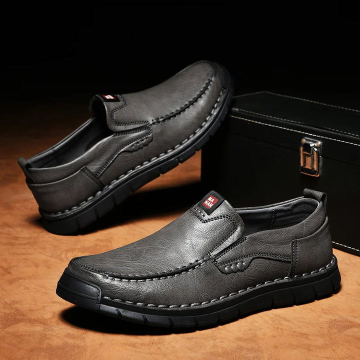 Pair of gray slip on loafers with stitched toe on a dark background