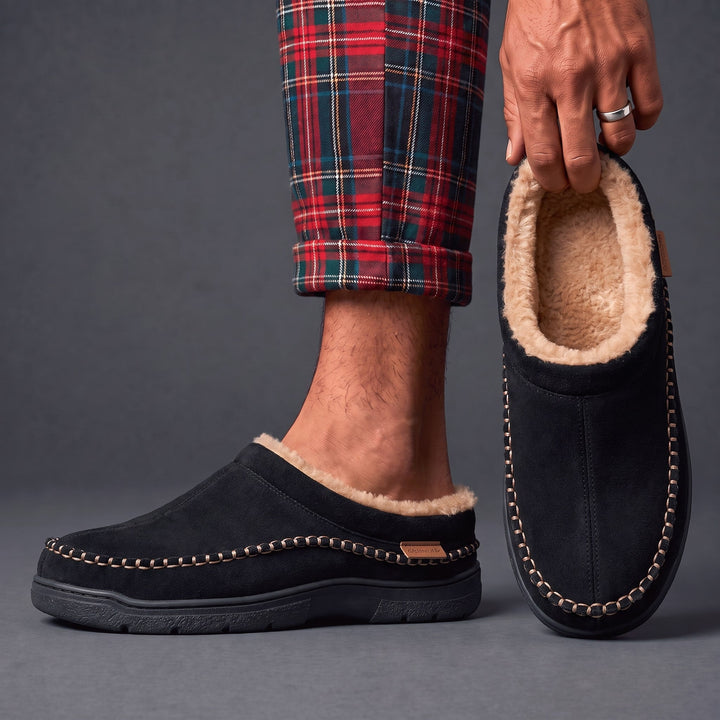 Black moccasin clog slippers worn with plaid pajama pants, one held up