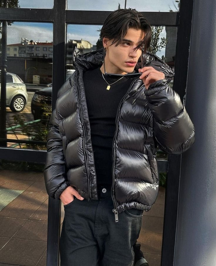 Black glossy puffer worn open over a black top, hood resting on the shoulders