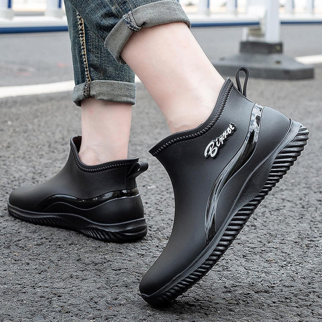 Black ankle rain boots in a walking pose on asphalt