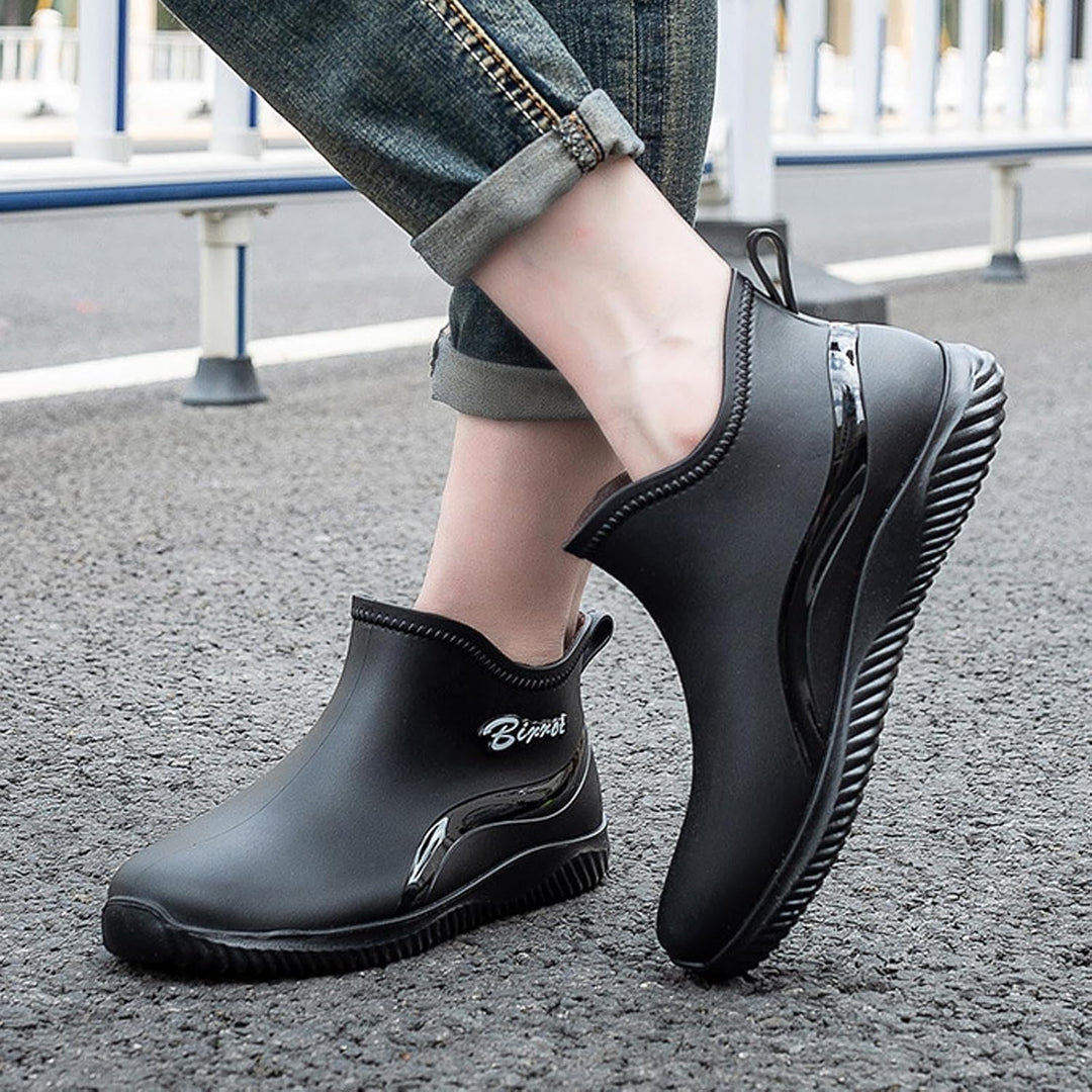 Black short rain boots worn with rolled jeans on wet pavement