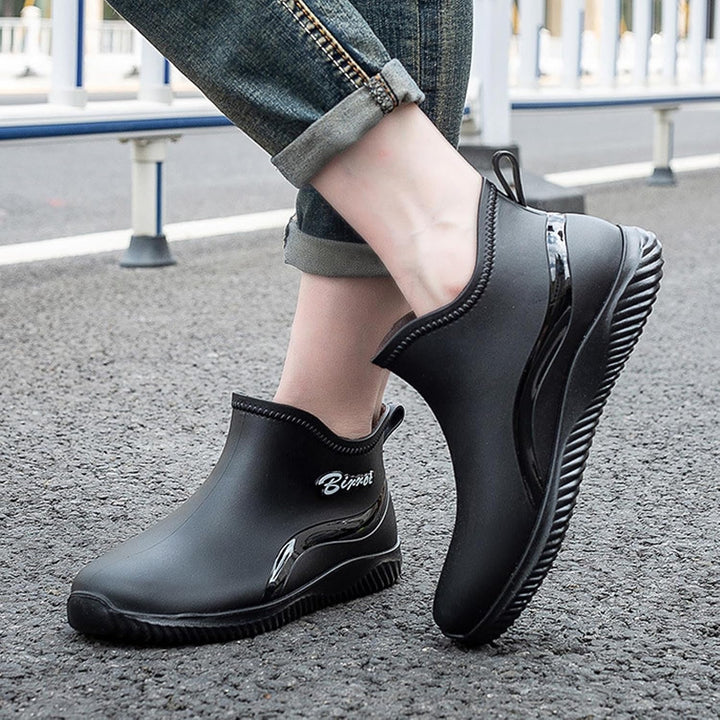 Black short rain boots worn with rolled jeans on wet pavement