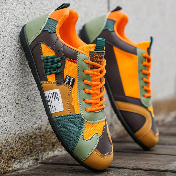 Orange color block lace-up sneakers leaning on a gray wall, angled side view