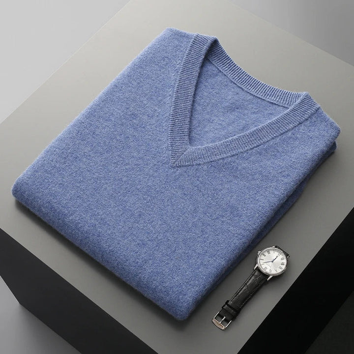 Blue V-neck knit vest folded on a gray block beside a watch