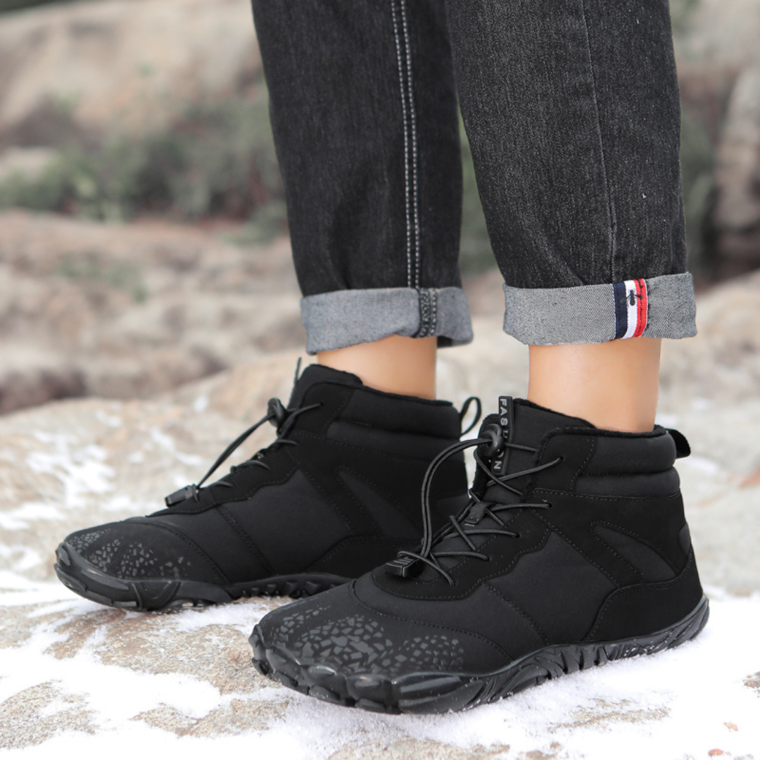Pair of black ankle boots worn on rocky ground with rolled up jeans