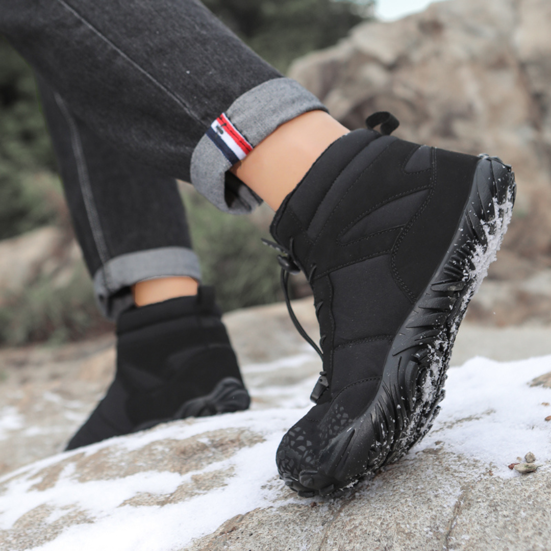 Black wide toe ankle boot worn on a snowy rock with cuffed jeans