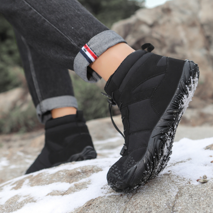 Black wide toe ankle boot worn on a snowy rock with cuffed jeans