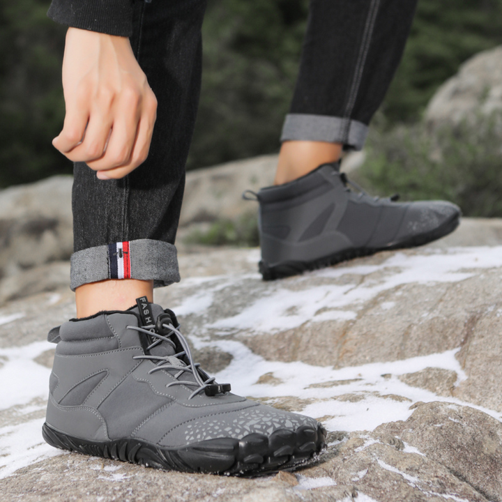 Gray ankle boot being pulled on, with a second boot resting on a rock