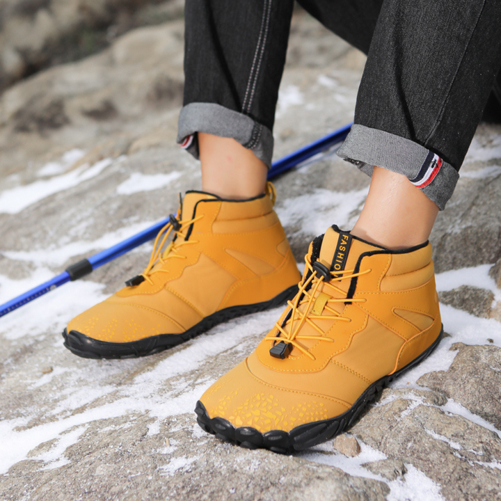 Pair of mustard ankle boots worn outdoors next to a blue trekking pole