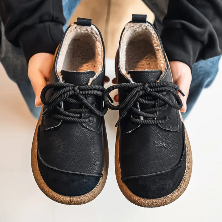 Pair of black lace up shoes held in hands, showing the fleece lined interior