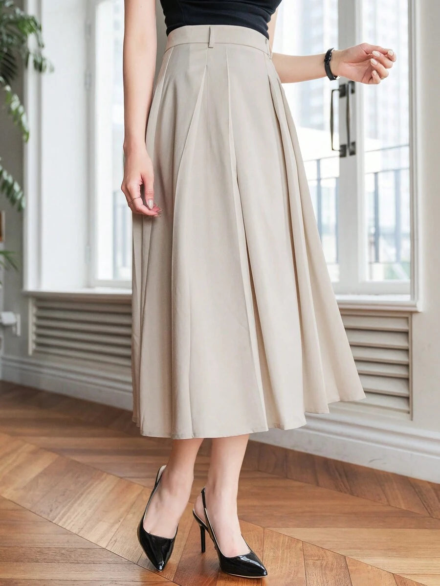 Beige pleated skirt in a bright room, model turned slightly with heels visible