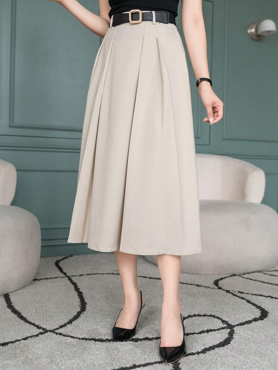 Pleated beige midi skirt with belt, model standing with one hand on hip