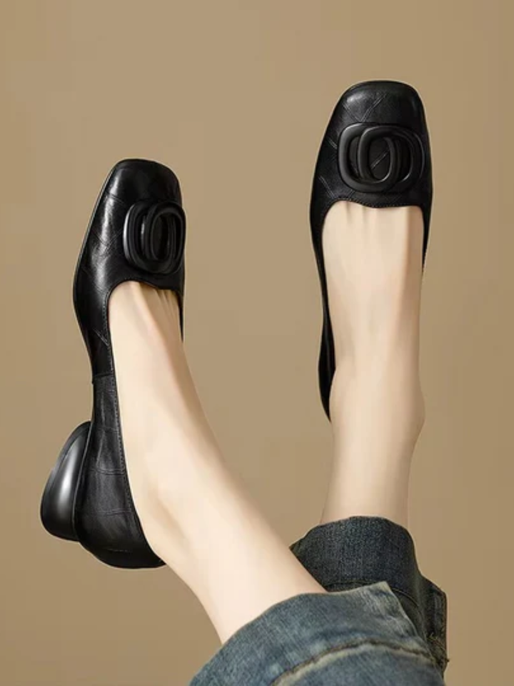 Black square toe ballet flats with ring detail on a beige backdrop, worn with cuffed jeans