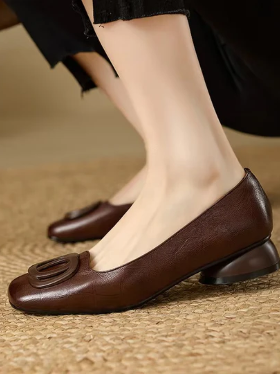 Close up of a brown square toe ballet flat with ring detail and low heel worn on a woven mat