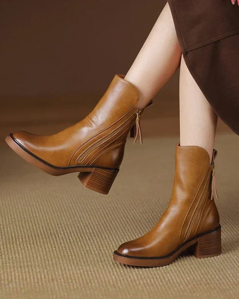 Tan block heel booties worn with a brown skirt on a woven rug