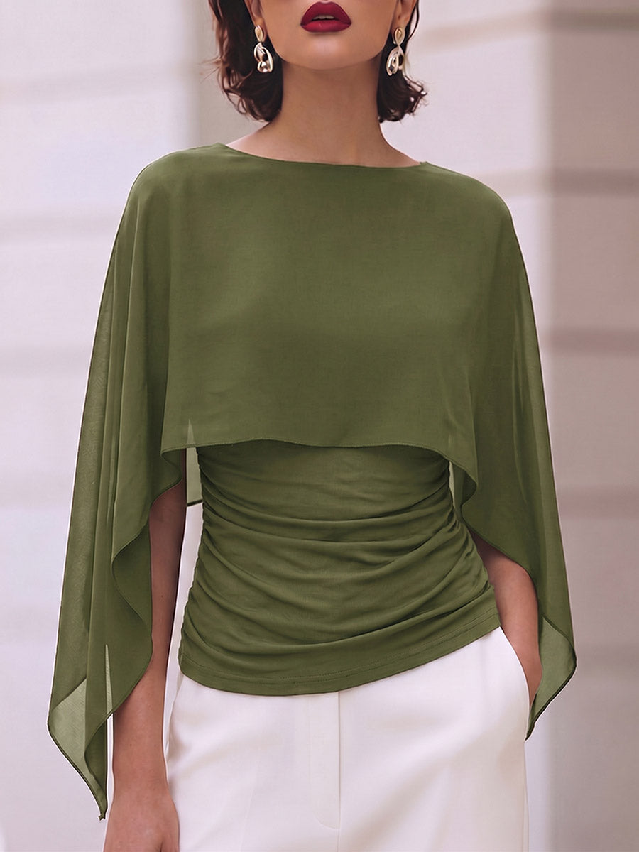 Olive cape-style top with pointed ends, worn with white pants