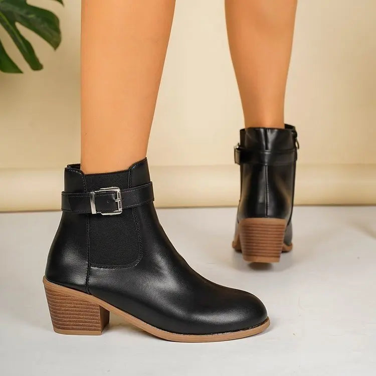 Black block heel Chelsea boots seen from behind with buckle strap, worn with bare legs