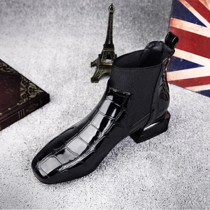 Women's Chelsea boots in black patent-look with croc texture, side view on gray surface