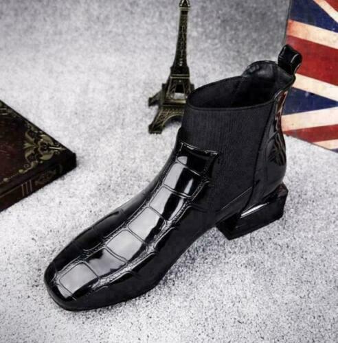 Black Chelsea boot angled on gray carpet beside small decorative props