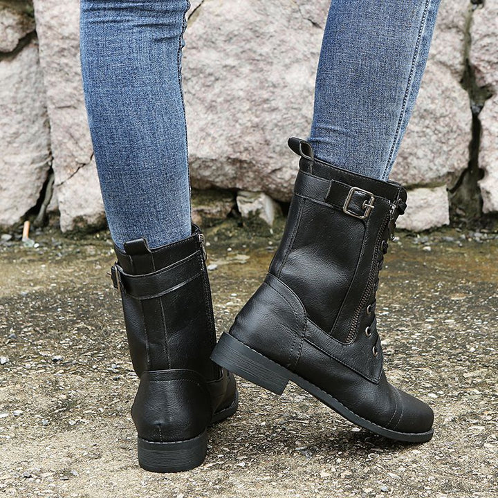 Black combat boot side view with buckle strap, worn with jeans