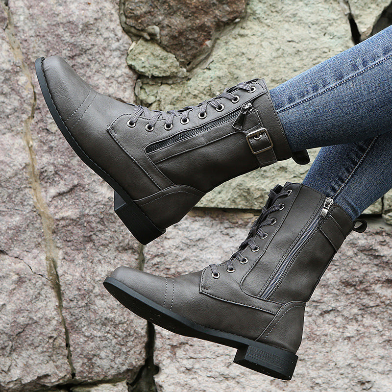 Women's combat boots in gray with lace up front and side buckle, worn with jeans against a stone wall