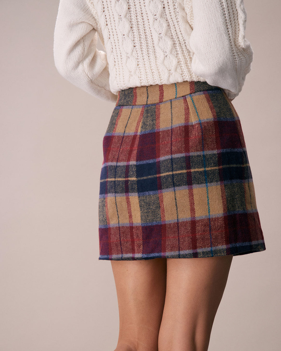 Rear three quarter view of the red plaid mini skirt on a model with a cream knit sweater