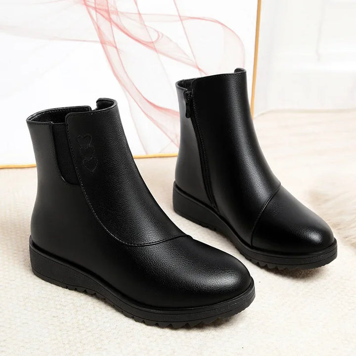 Pair of black flat ankle boots with side zip and round toe on a light backdrop